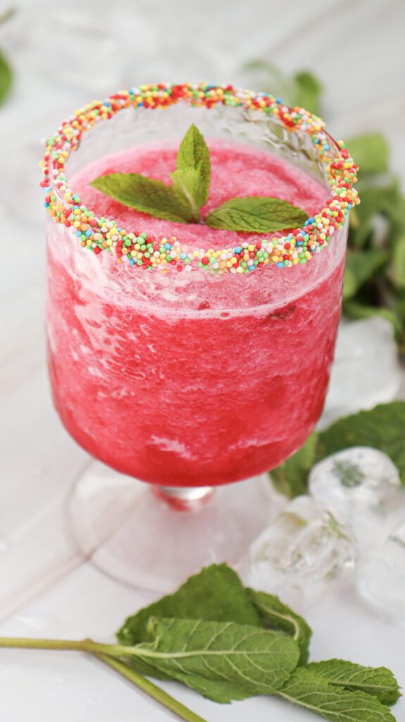 Watermelon slushie in a glass with sprinkles on the rim