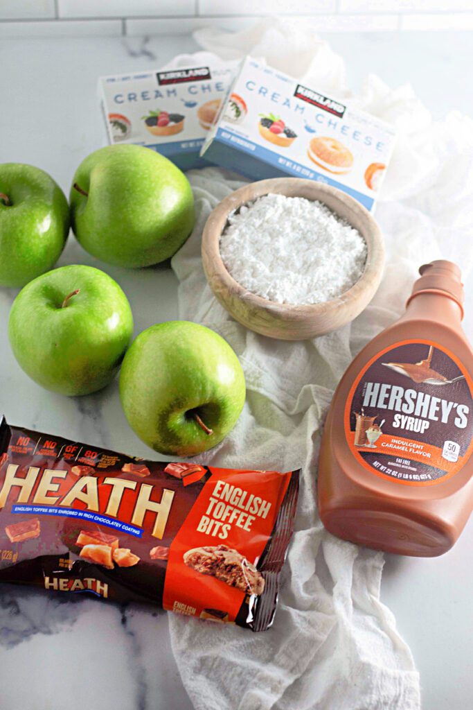 Ingredients of toffee apple dip - green apples, hersheys caramel syrup, heath toffee bits, powdered sugar, cream cheese