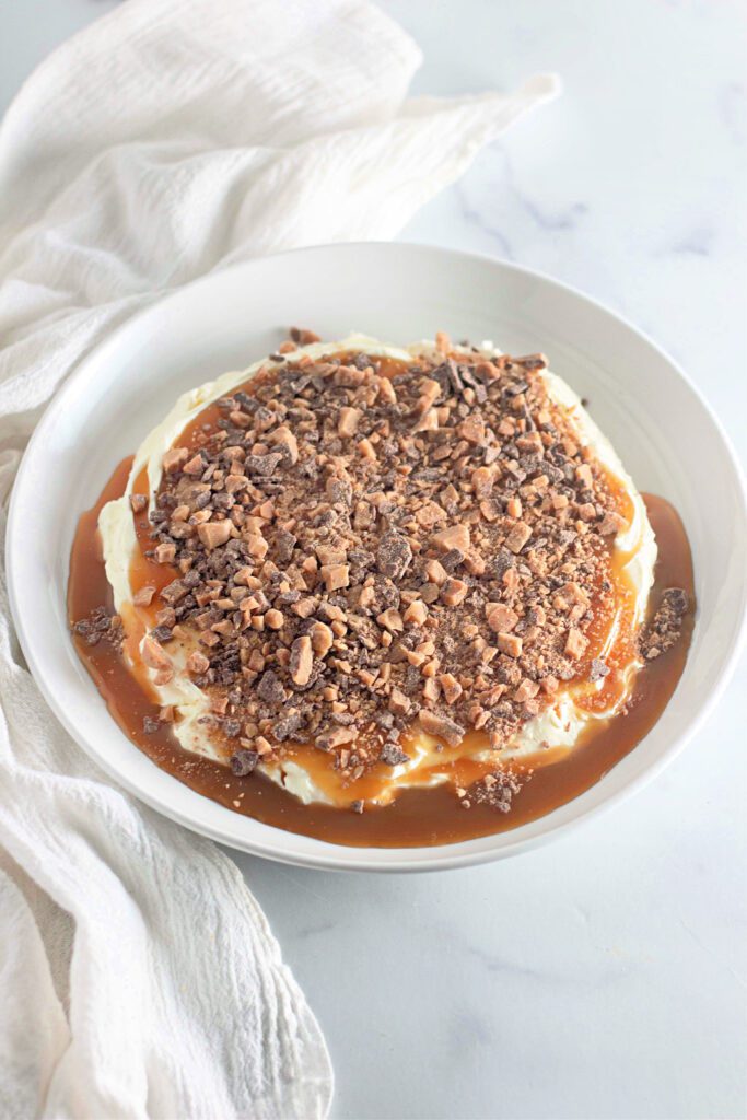 Toffee apple pie dip in a big bowl with cream cheese on top and toffee bits