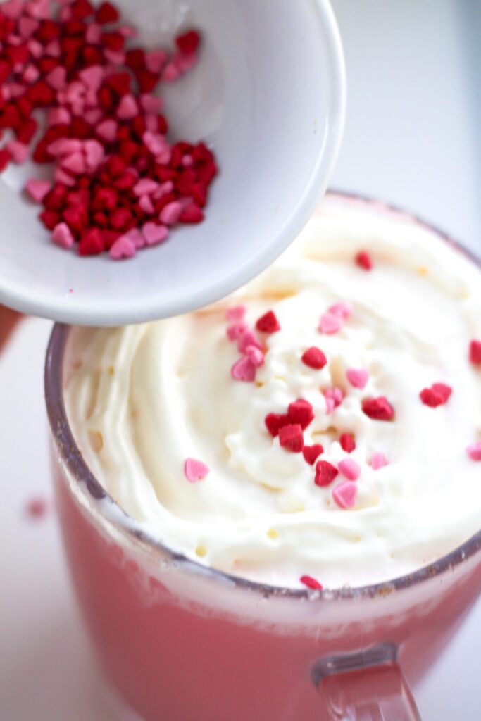 Adding sprinkles to whip cream of red velvet hot chocolate drink