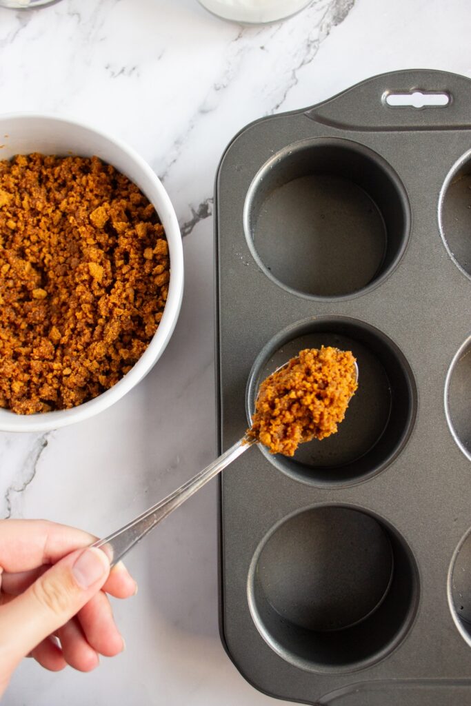 Adding the biscoff and butter mixture into mini cheesecake pans