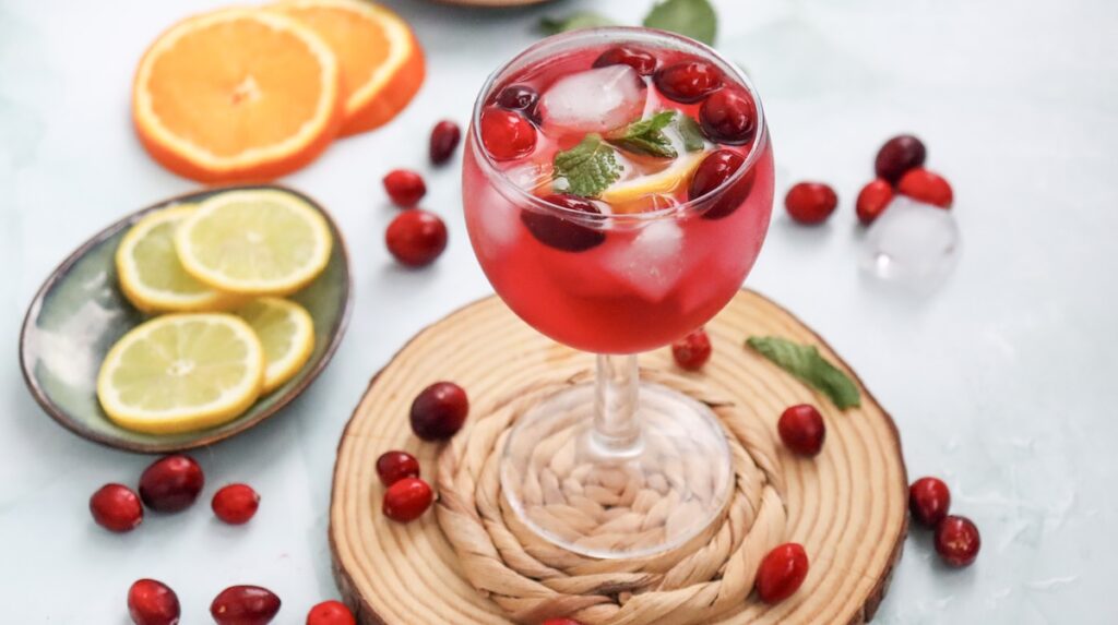 non alcoholic cranberry spritzer in a glass topped with cranberries and slices of lemons and oranges on the side
