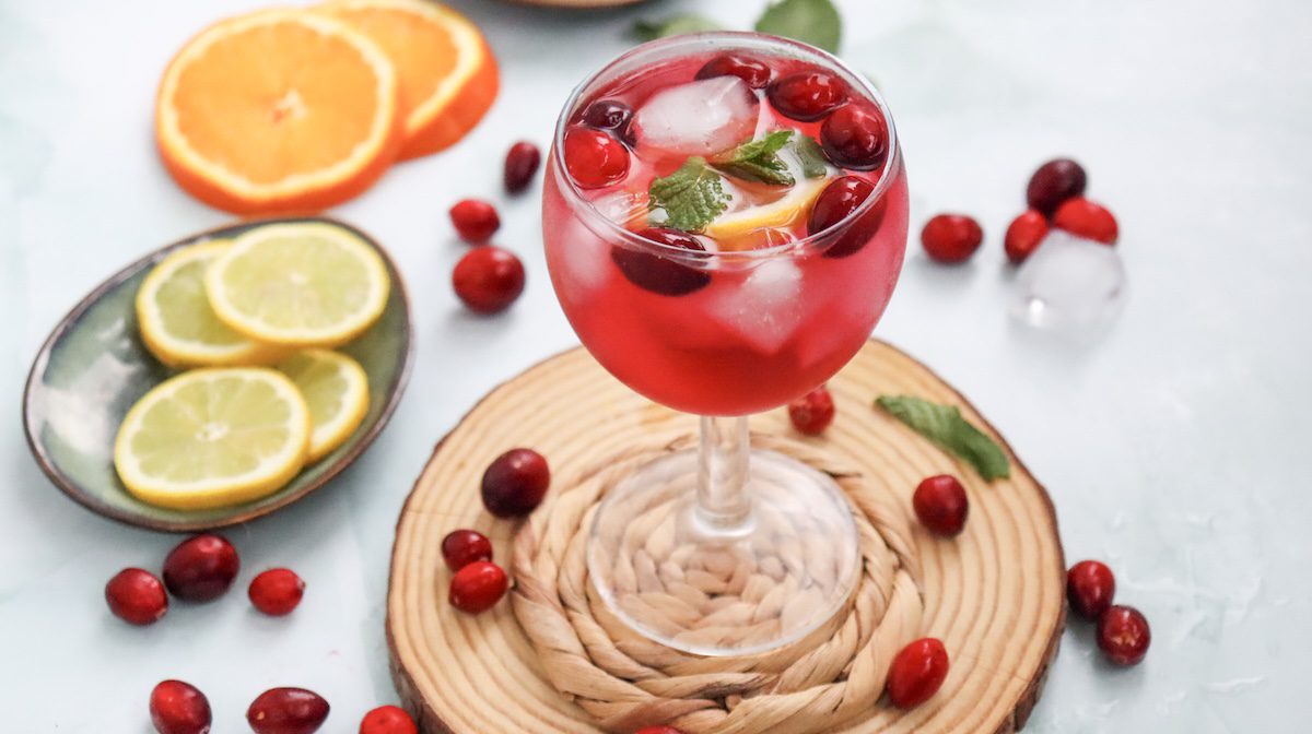 non alcoholic cranberry spritzer in a glass topped with cranberries and slices of lemons and oranges on the side
