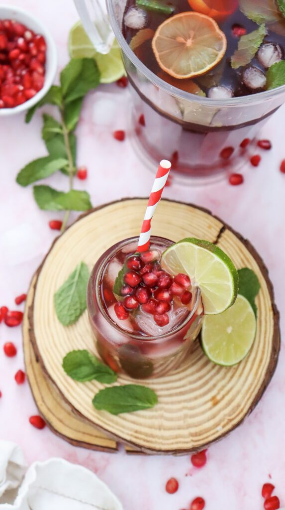 A glass of pomegranate fizz with ice and pomegranate seeds topped with mint and lime slices