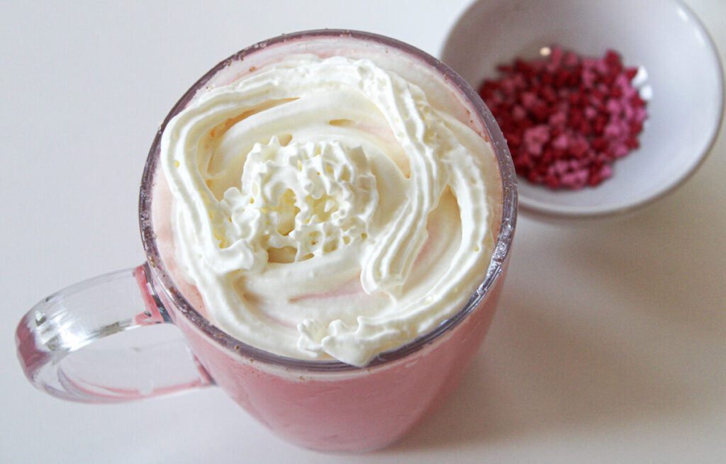 Adding whipped cream to a mug of red velvet hot chocolate