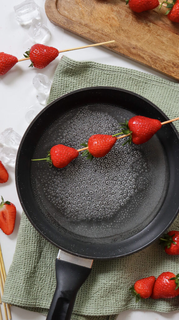 Dipping strawberries in skewers in hot sugar mixture