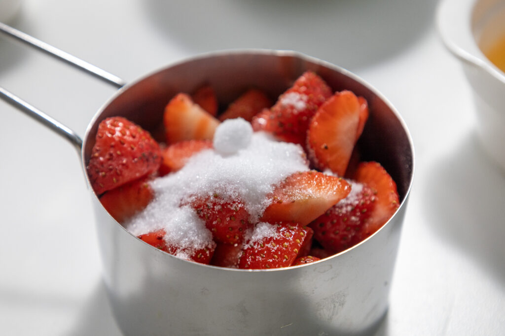 Strawberries in a measuring cup with granulated sugar