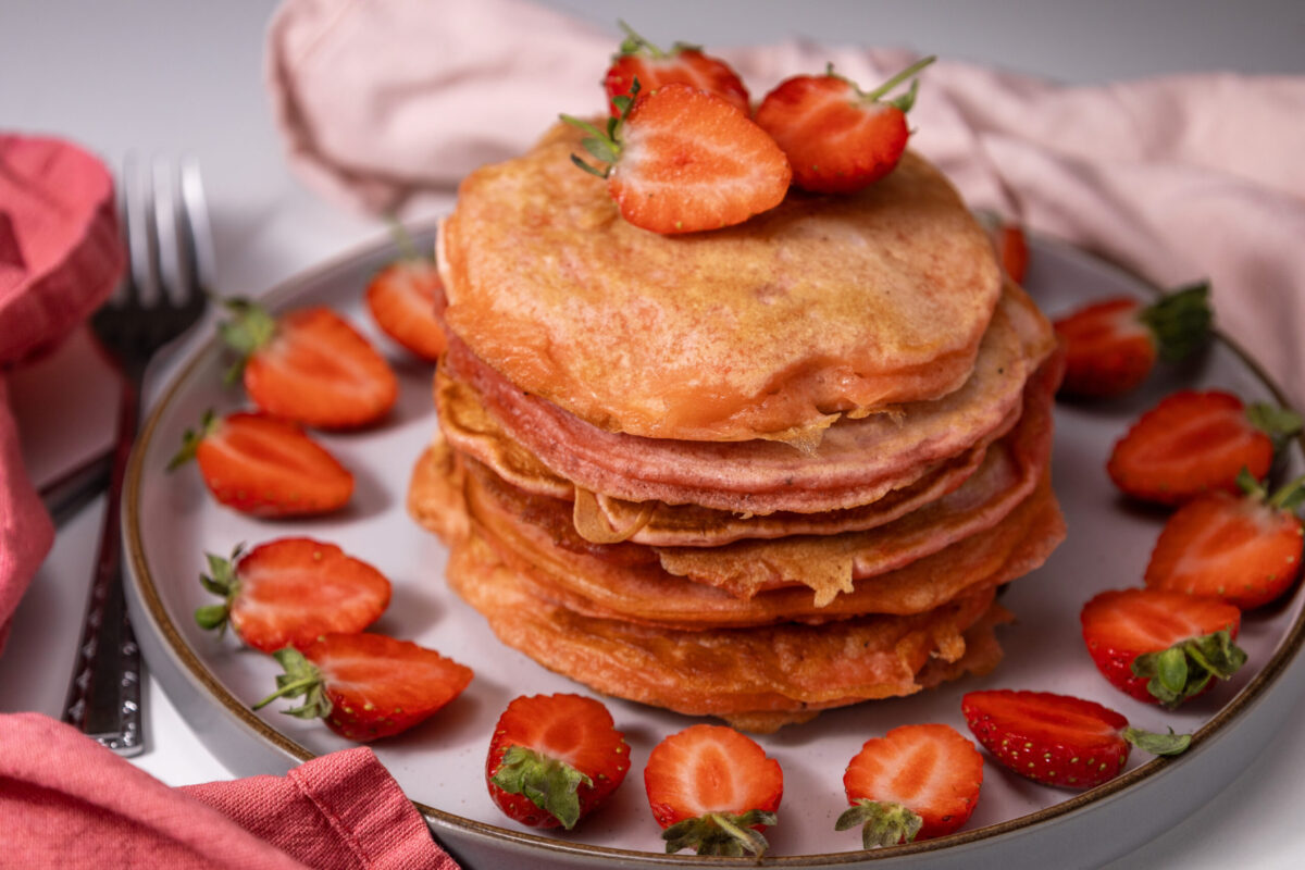 Stack of strawberry pancakes on a plate with strawberry toppings