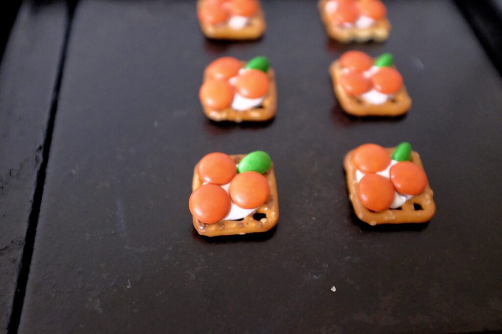 adding orange m&ms on top of the pretzel and cut green m&ms as stem