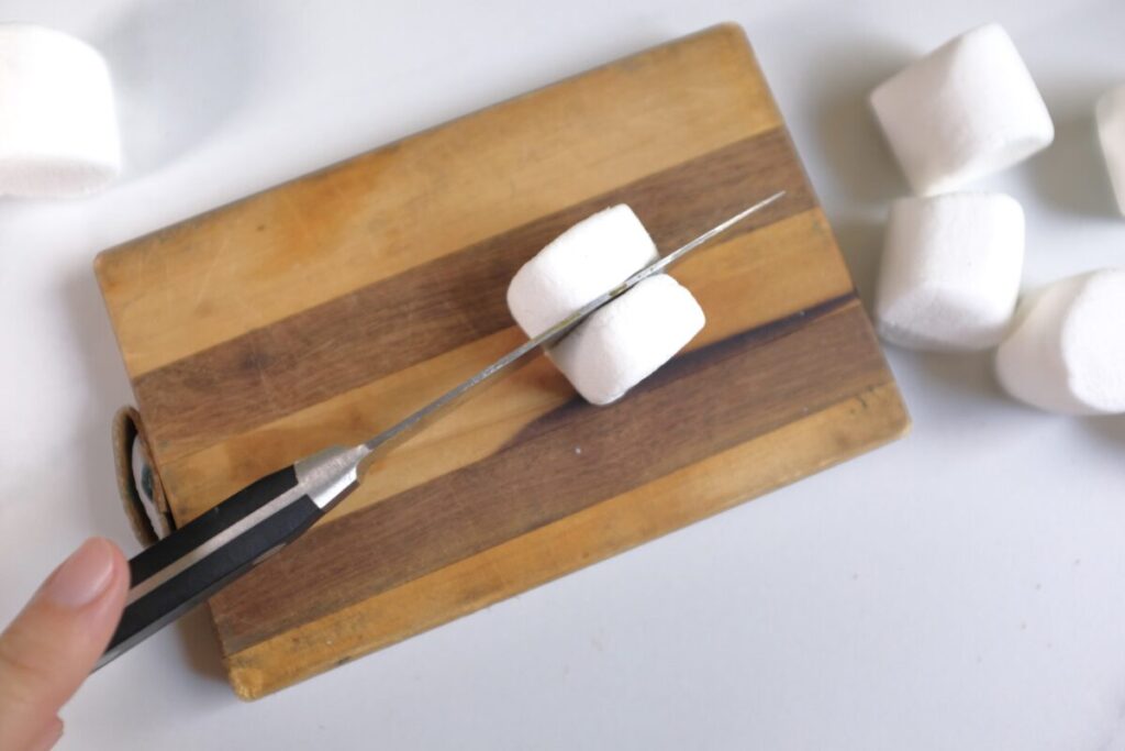 cutting marshmallows to half using a knife and a wooden chopping board