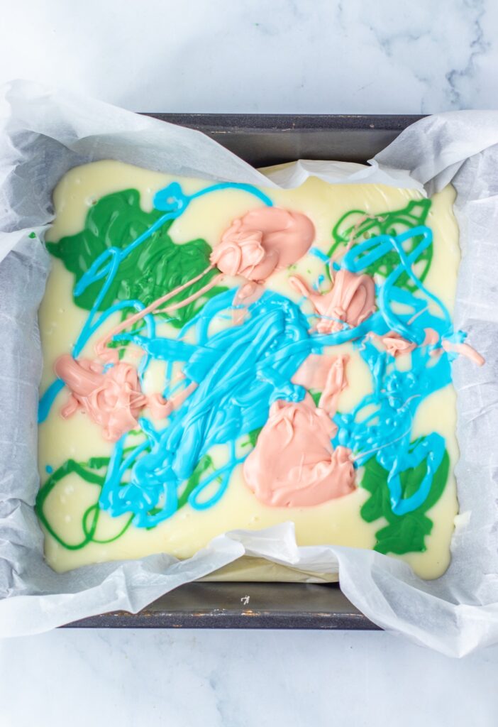 melted white chocolate in a pan with melted green, pink and blue chocolate swirled in