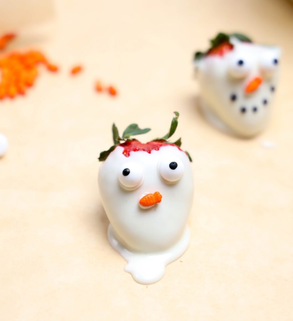 a strawberry dipped in white chocolate with eyes and a carrot nose sprinkles added to look like a snowman