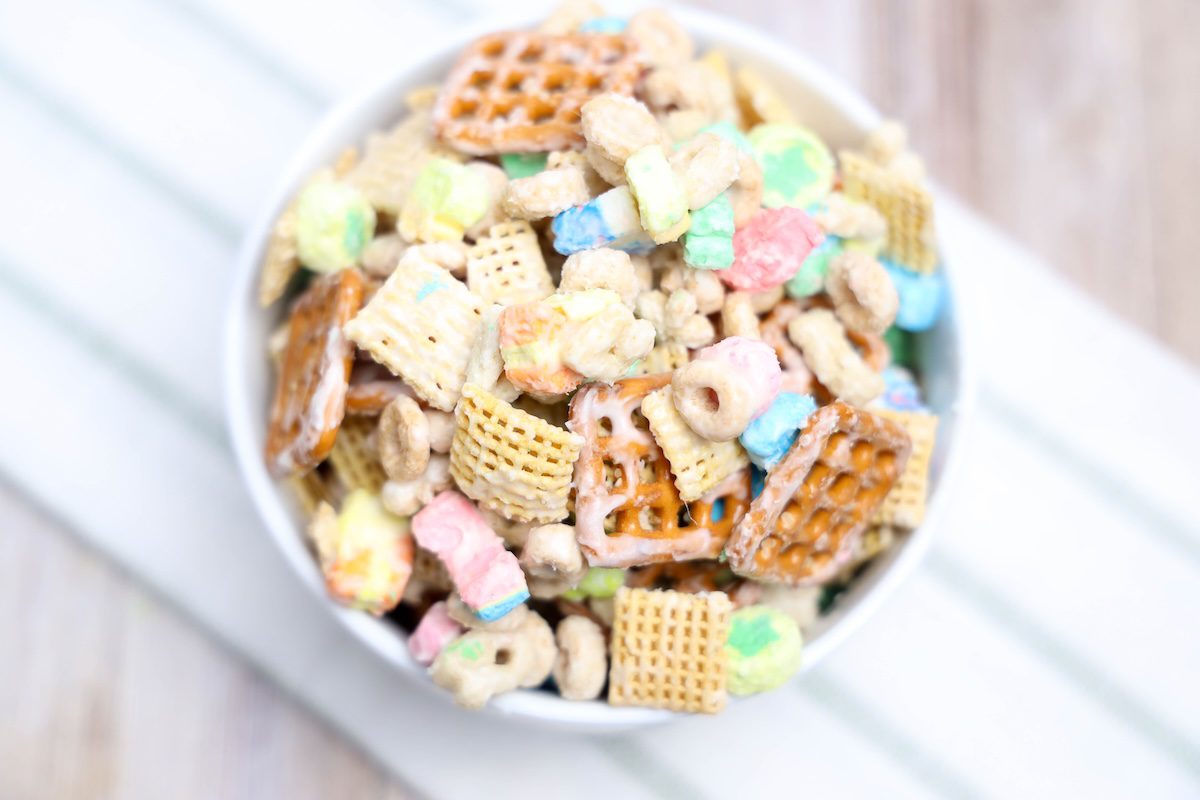 Overhead view of the white bowl on a striped towel, showing the full variety of snack mix ingredients and pastel colors.