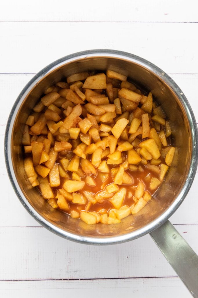 Cooked apple filling in a saucepan, showing softened apples coated in a caramelized cinnamon-sugar mixture