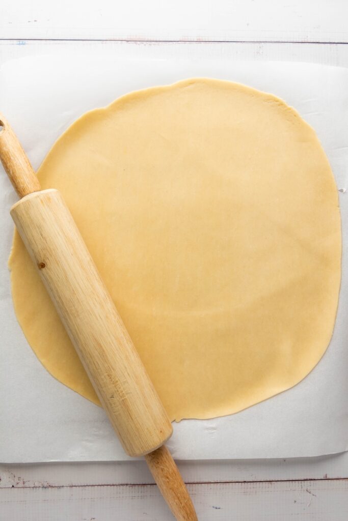 Rolled out pie dough on parchment paper with a rolling pin, forming a large even circle ready to be cut