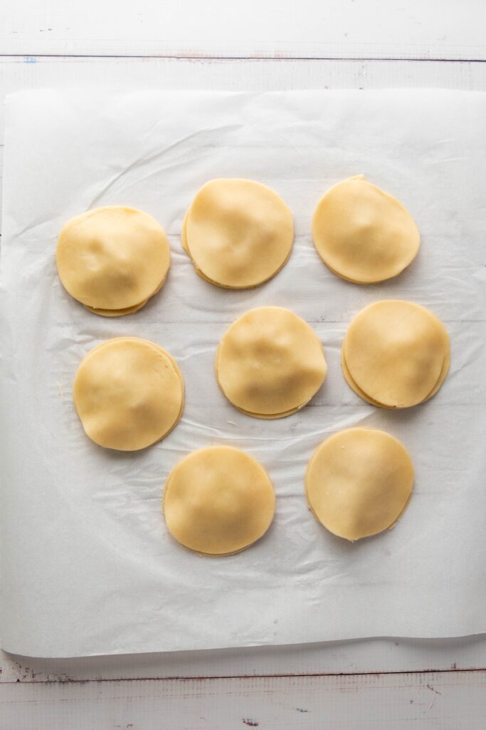 Dough circles pressed together and sealed into rounded hand pies, resting on parchment paper before baking
