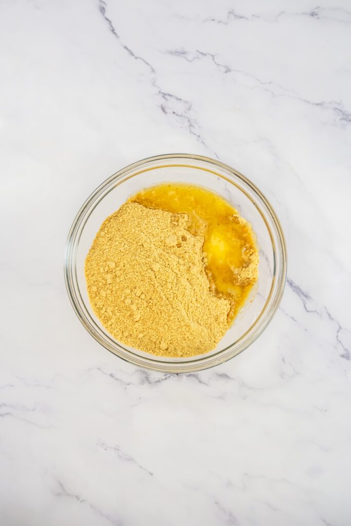 Mixing bowl filled with graham cracker crumbs and melted butter, ready to be combined for the crust