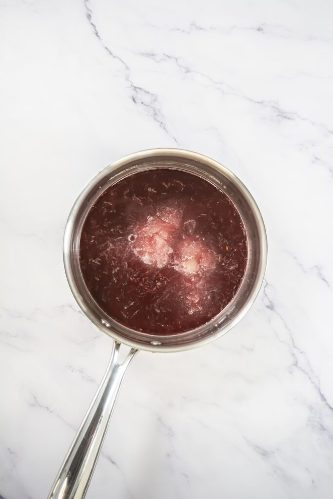 Blood orange jelly mixture simmering in a saucepan with visible citrus pulp and dissolved gelatin