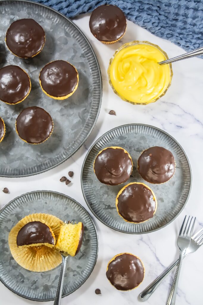 Cross-section view of a Boston Cream Pie cupcake with a bite taken out, showing moist yellow cake and a generous custard center