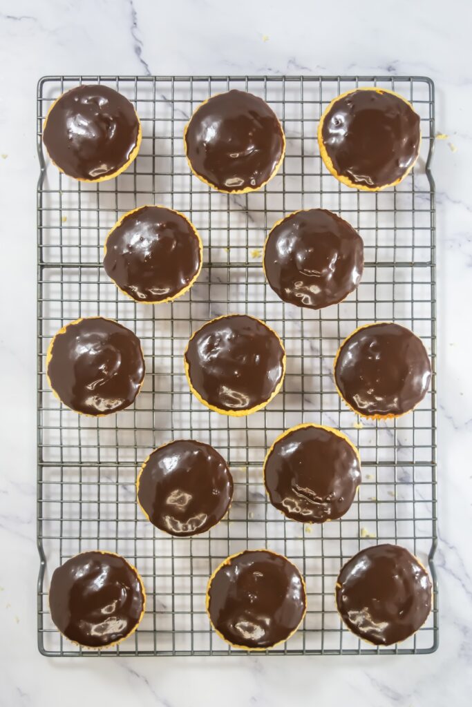 Cupcakes topped with rich, glossy chocolate ganache, set neatly on a wire cooling rack