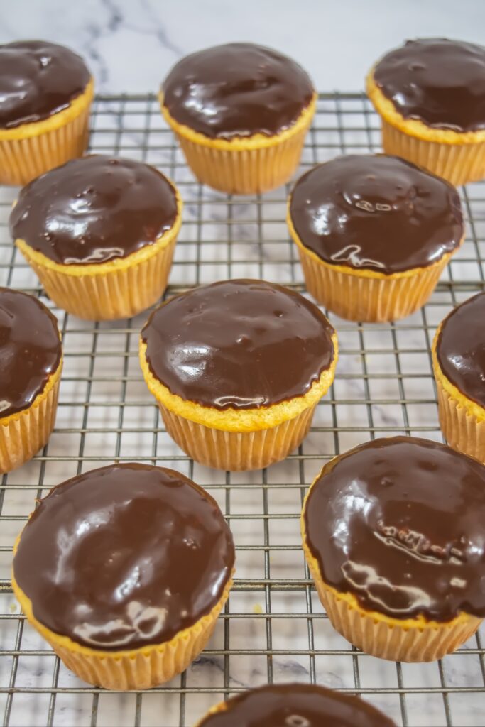 Side view of the finished Boston Cream Pie cupcakes, showing the shiny chocolate topping and yellow cupcake base