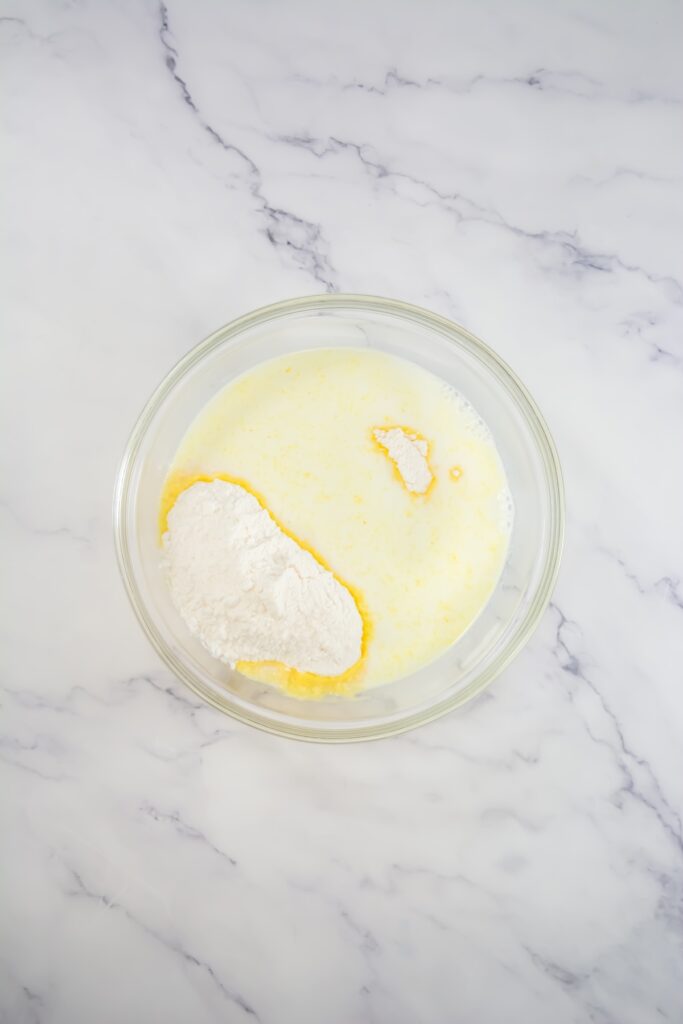 Unmixed vanilla pudding powder and milk in a clear glass bowl before stirring, set on a white marble background