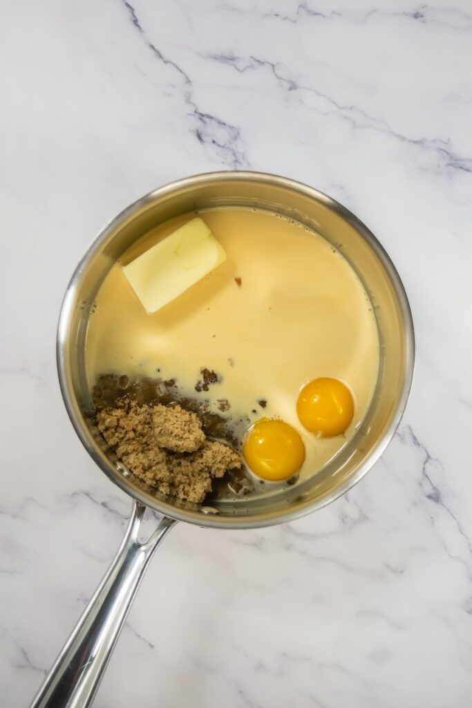 Saucepan containing butter, brown sugar, sweetened condensed milk, and egg yolks before cooking the German chocolate frosting