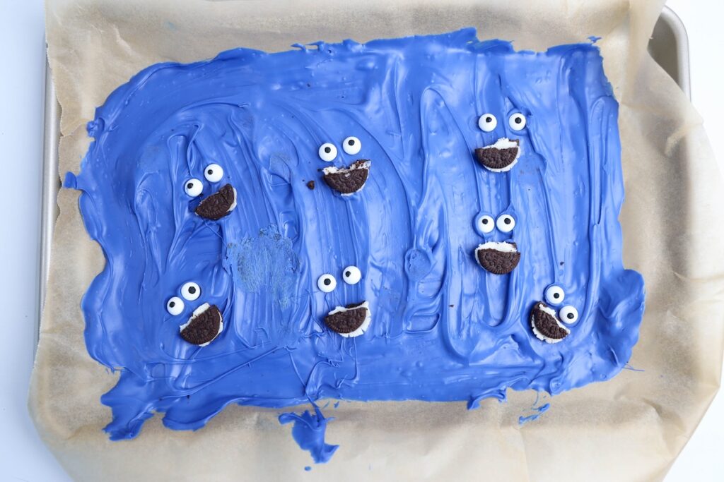 The blue candy base on the tray decorated with pairs of candy eyes and halved sandwich cookies, forming playful Cookie Monster-like faces