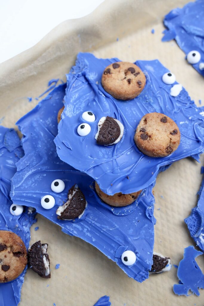 Broken pieces of Cookie Monster bark on parchment, featuring googly eyes, cookie mouths, and embedded mini chocolate chip cookies