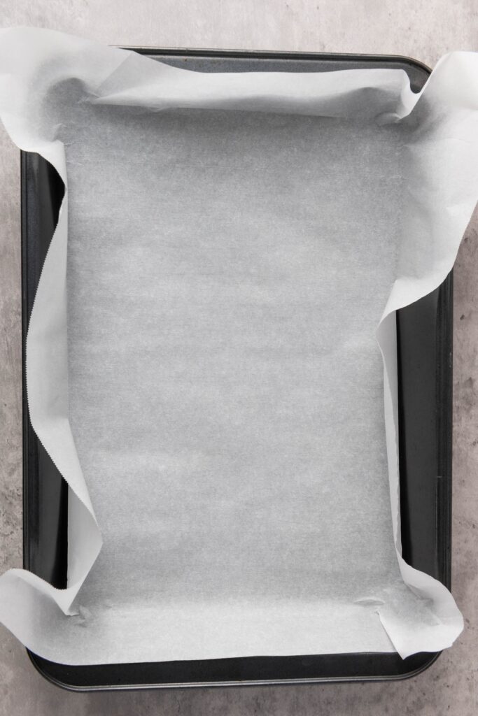 A rectangular baking pan lined with parchment paper, ready for chocolate bark preparation