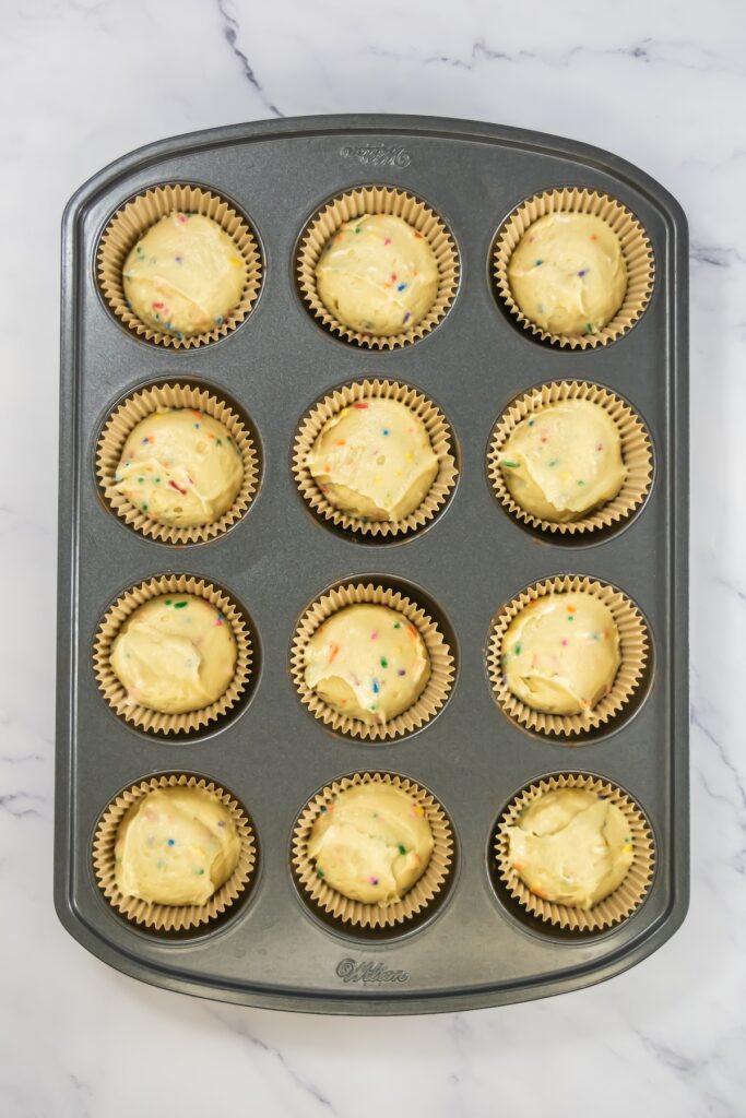 Cupcake pan filled with raw funfetti cupcake batter in paper liners, ready to be baked