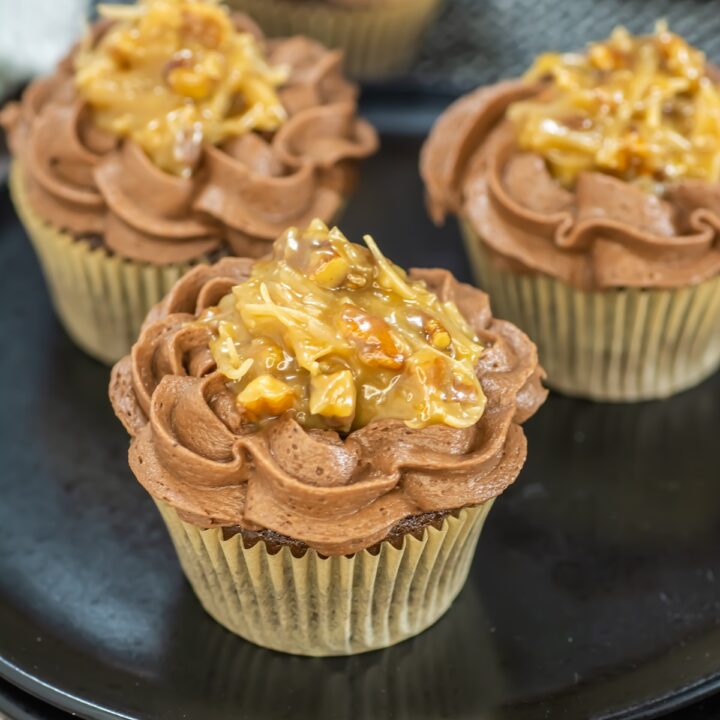 Close-up angled view of German chocolate cupcakes on a black plate, featuring rich chocolate frosting and a golden coconut-pecan topping