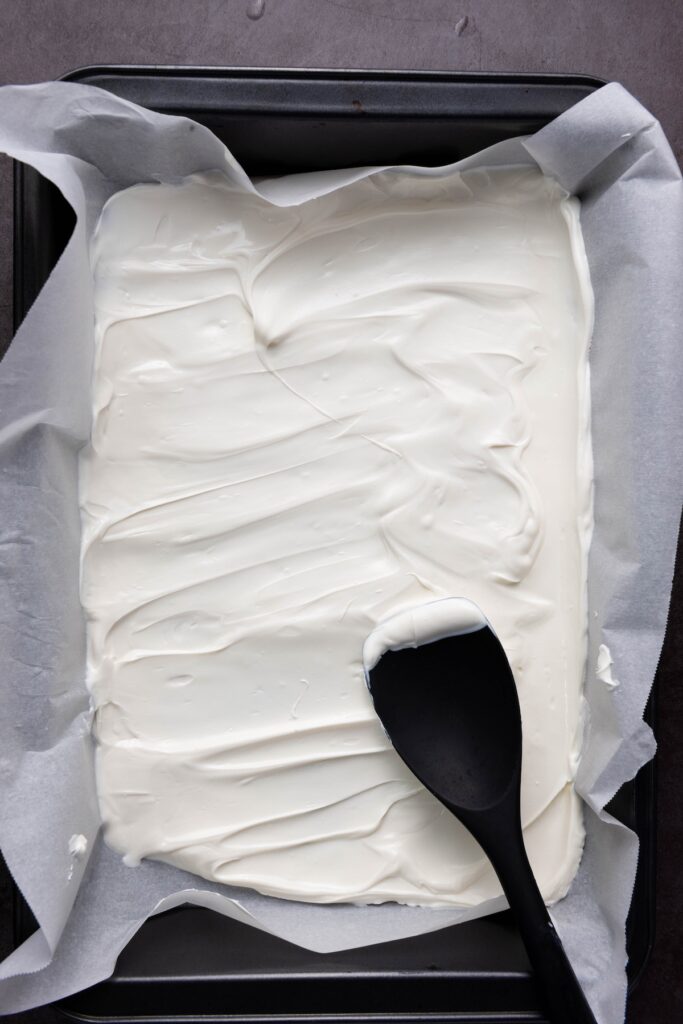White chocolate spread evenly in a parchment-lined baking tray, with a black spatula resting in the corner
