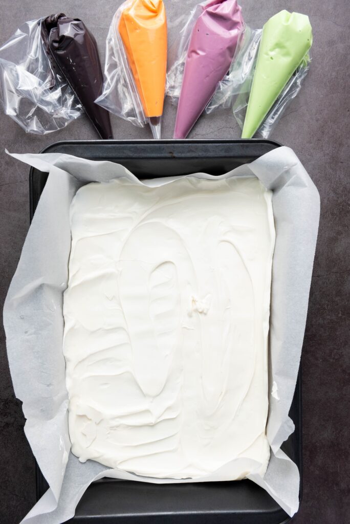 Tray of white chocolate topped with drizzled colored chocolate in Halloween hues of orange, purple, green, and black