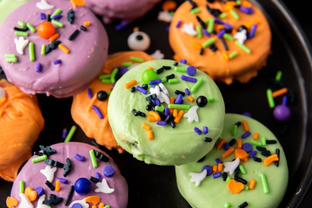 A plate full of decorated Halloween Oreos with vibrant sprinkles, eyeballs, and various fun Halloween toppings