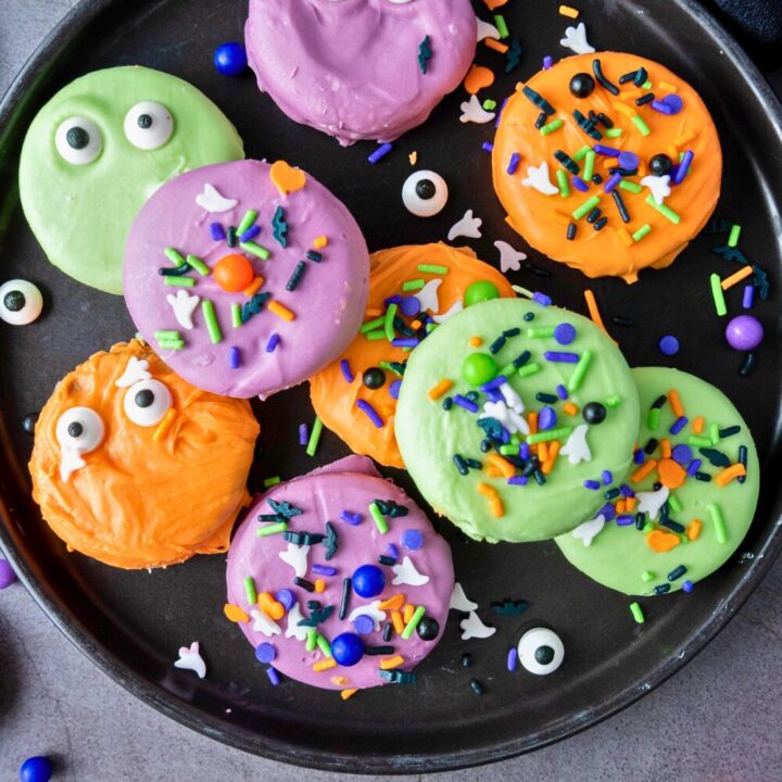 A plate full of decorated Halloween Oreos with vibrant sprinkles, eyeballs, and various fun Halloween toppings