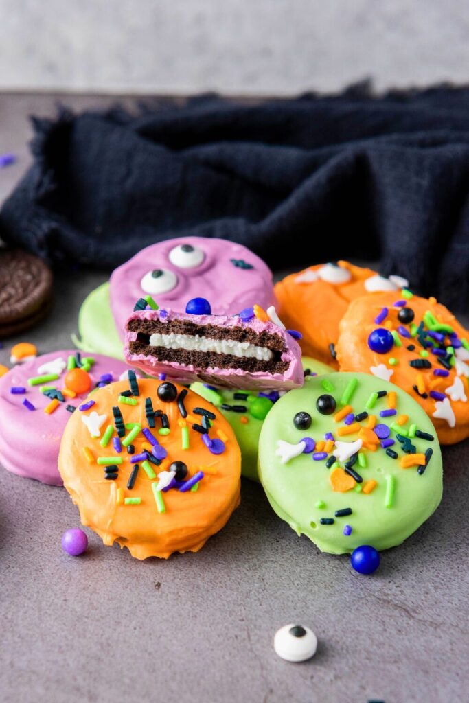 A stack of Halloween-dipped Oreos, one with a bite taken out to reveal the classic white creme center inside the colorful chocolate shell
