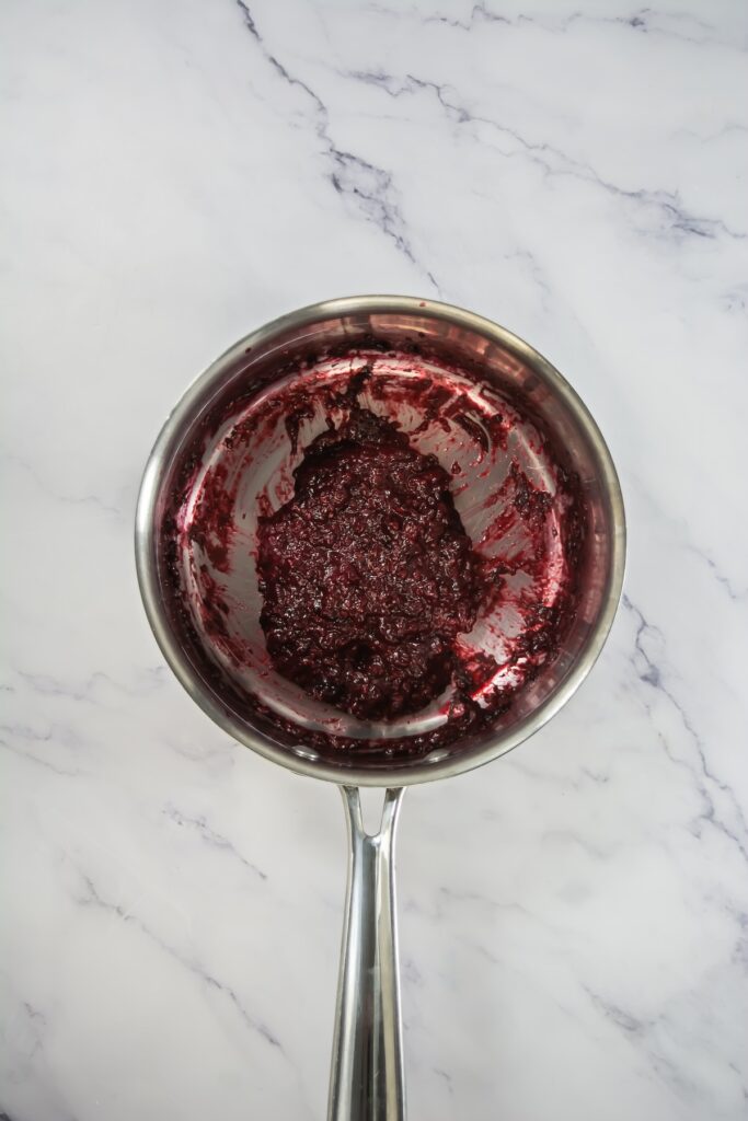 A large metal bowl of light purple berry frosting, fully mixed and swirled with specks of berries throughout