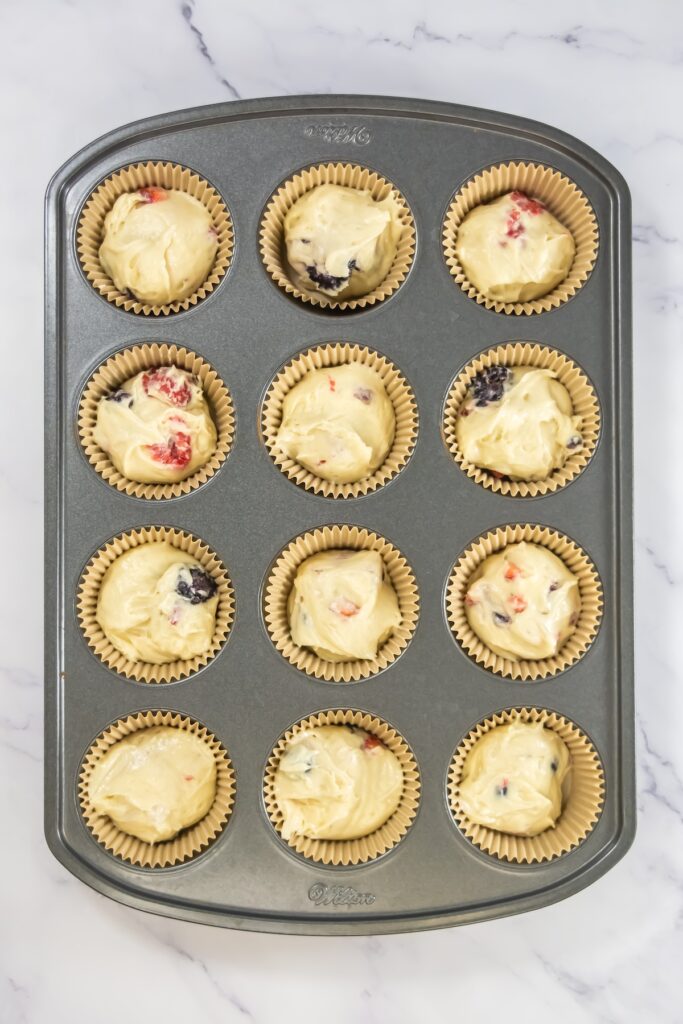 Muffin tin filled with cupcake liners and scoops of mixed berry batter, ready to go into the oven