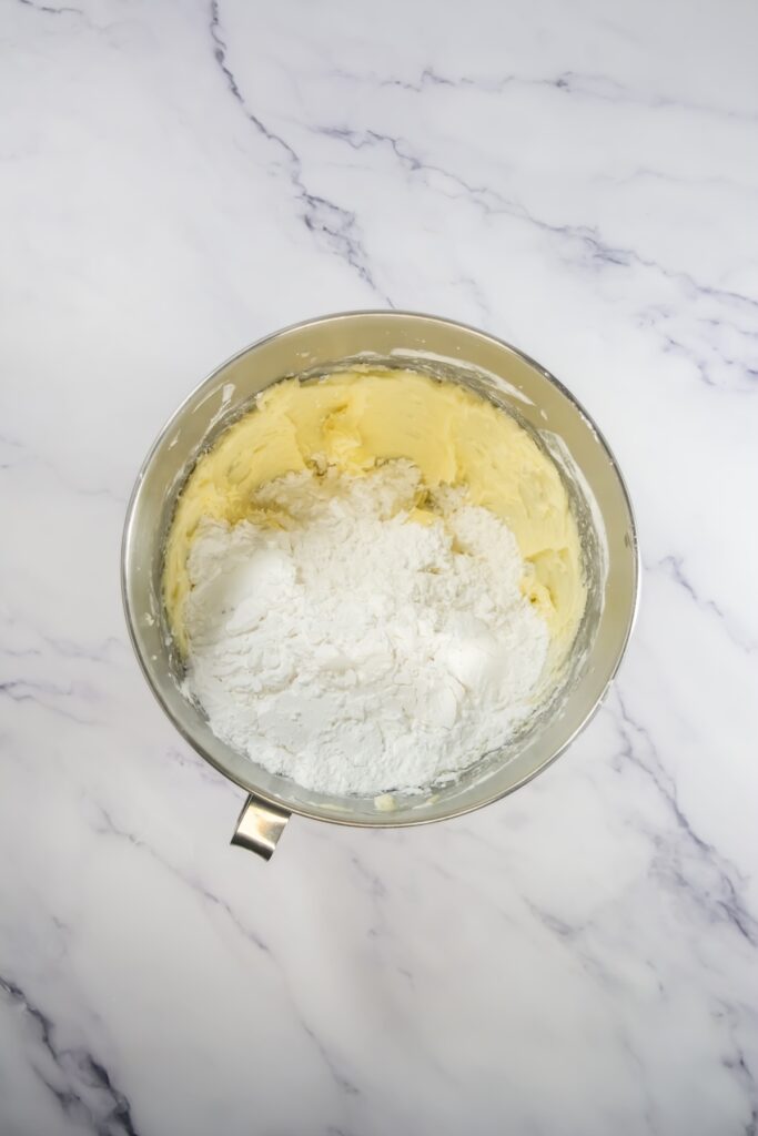 Frosting mixture in progress, with powdered sugar being combined into creamed butter in a large mixing bowl