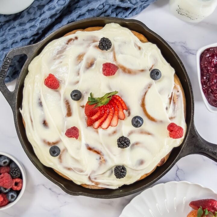 Overhead view of the fully frosted skillet of sweet rolls, garnished with fresh strawberries, raspberries, blackberries, and blueberries for a colorful finish