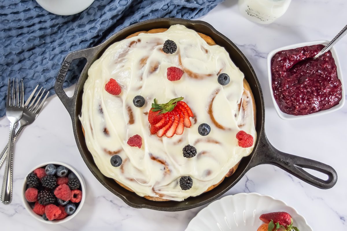 Overhead view of the fully frosted skillet of sweet rolls, garnished with fresh strawberries, raspberries, blackberries, and blueberries for a colorful finish