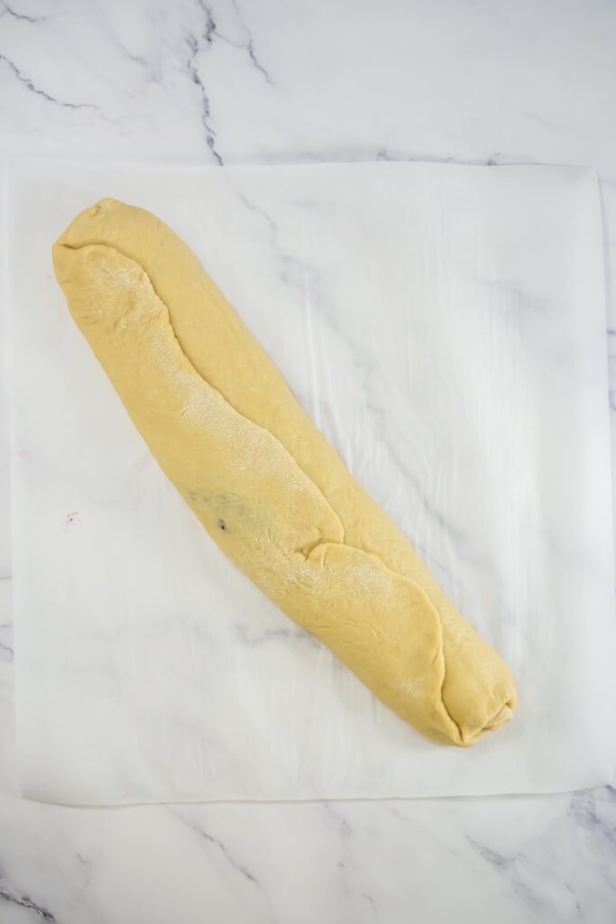 Rolled dough has been tightly rolled into a log with the berry filling swirled inside, ready for slicing