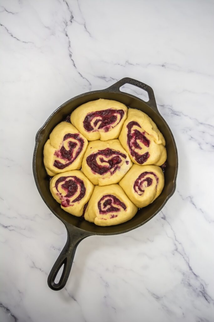 Mixed berry sweet rolls after proofing, now puffed up and filling the skillet more snugly before baking
