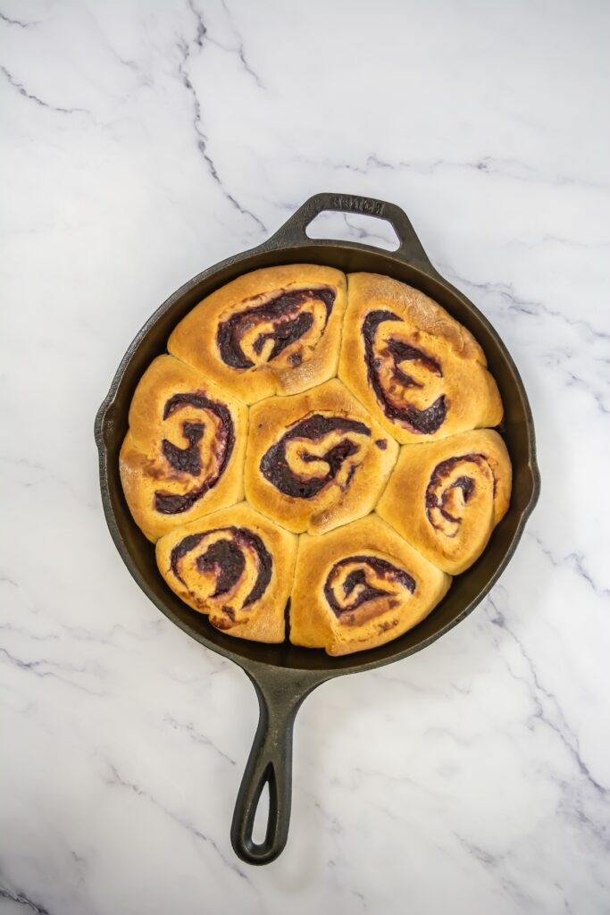 Baked golden brown mixed berry sweet rolls in a skillet, with visible swirls of dark berry filling and a soft texture