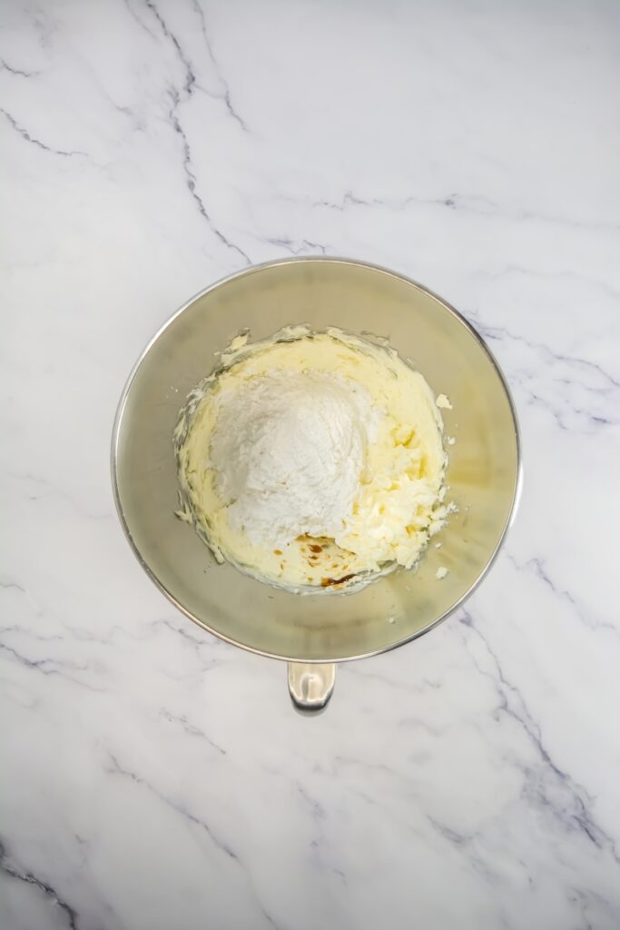 Mixing bowl showing butter, cream cheese, powdered sugar, and vanilla extract before being blended into frosting