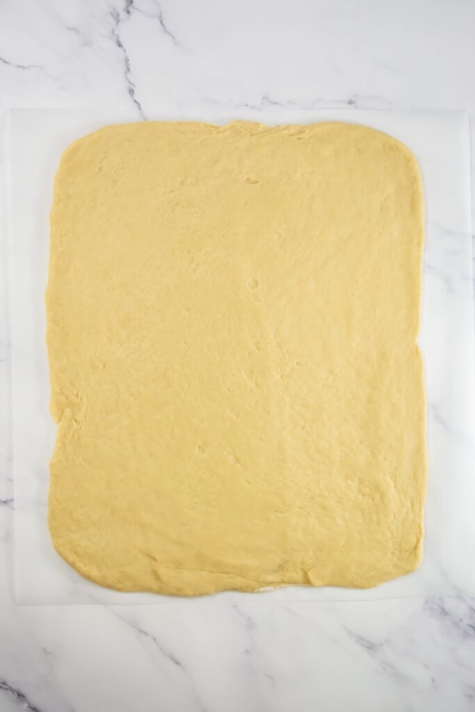 Rolled-out sweet roll dough in a large rectangle shape on parchment paper, prepped for filling