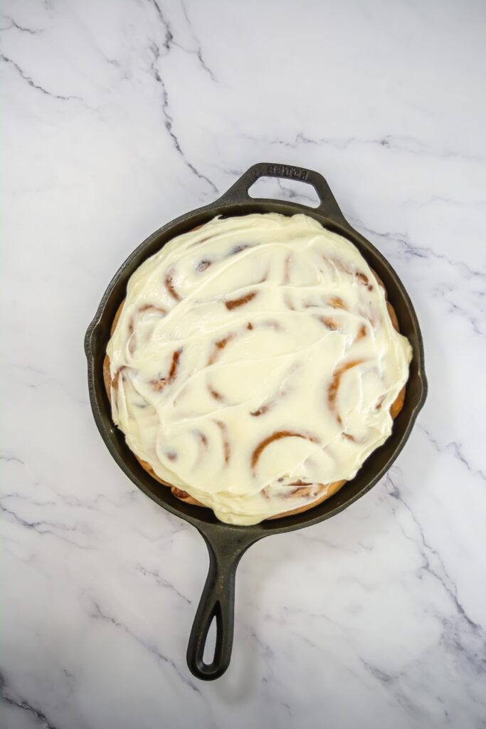 The finished sweet rolls covered in a generous layer of creamy white icing, slightly melting into the swirls