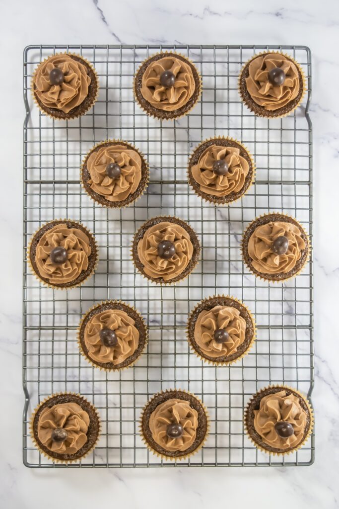 Fully decorated mocha cupcakes each topped with a chocolate-covered espresso bean, displayed evenly on a wire rack