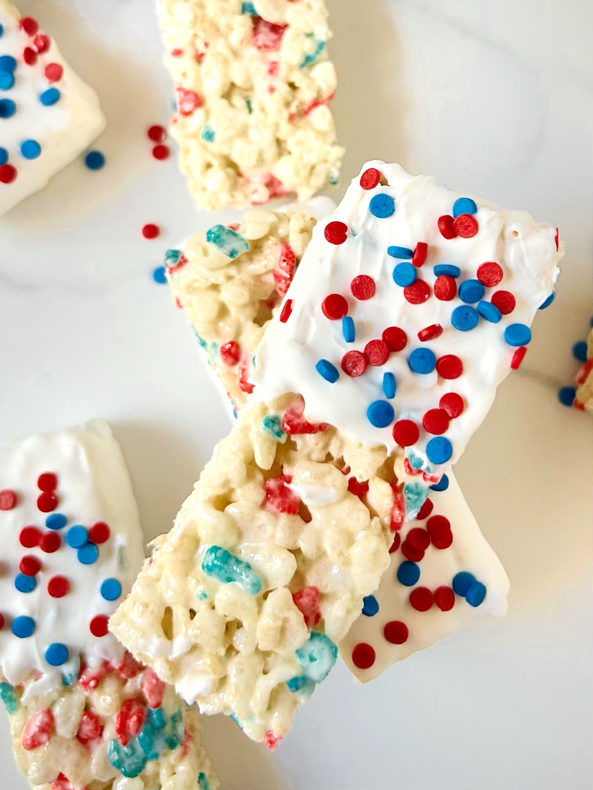 Close-up of red, white, and blue sprinkle-topped Rice Krispie treats, half-dipped in white candy coating for a festive, patriotic look